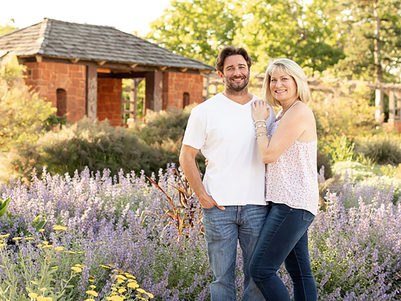 middle aged couple standing in front of blooms and home